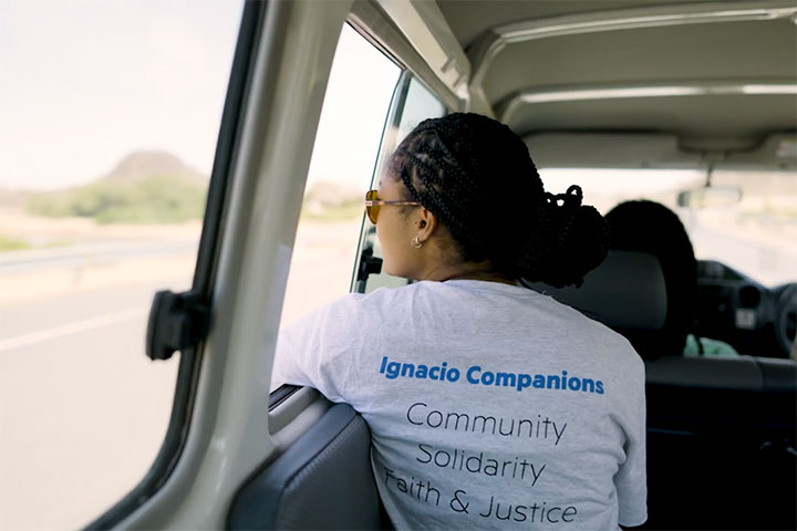 A student in a vehicle with a shirt that reads Ignacio Companions Community Solidarity Faith and Justice