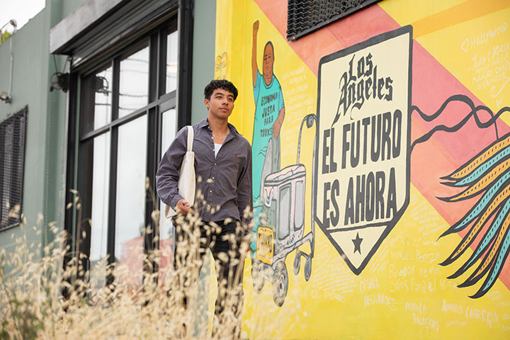 Elias Herrera walking past a mural that reads Los Angeles el futuro es ahora